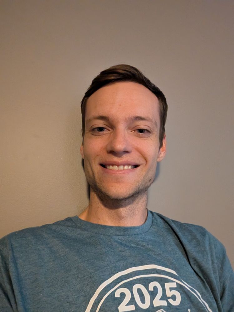 Selfie of a man in his 30s with a pleasant smile. His shirt reads 2025. 