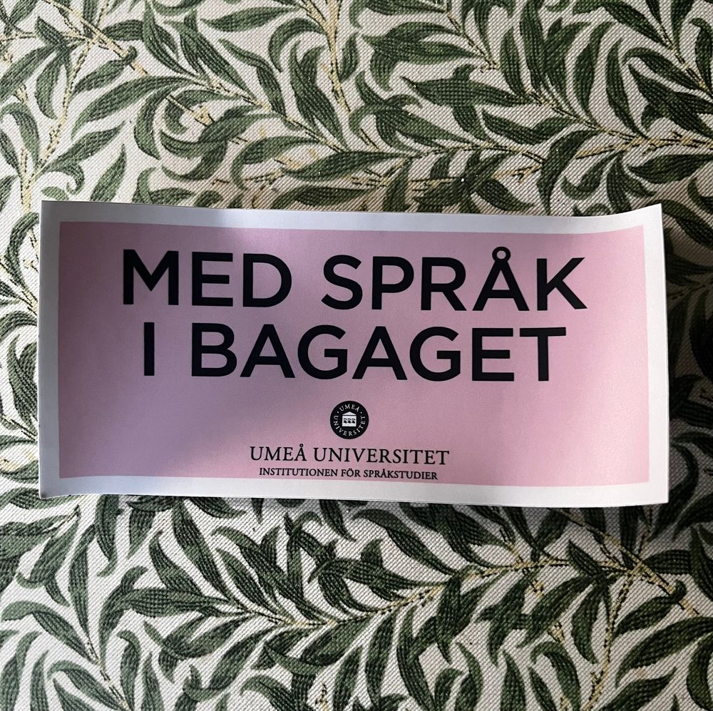 Picture of a pink sticker with the text “Med språk i bagaget”.