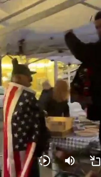 person stands in line for food with an American flag draped over their shoulders