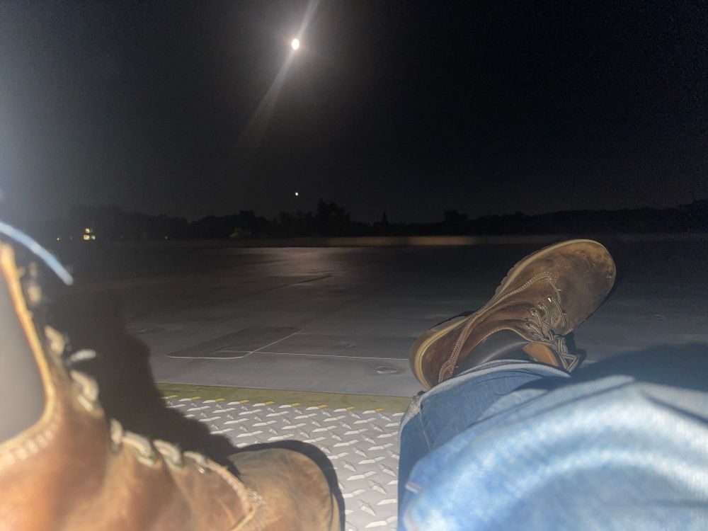 a photo of flagstaff’s outstretched leg and boot as he sits on the roof. in the sky is a very bright but not quite full moon. 