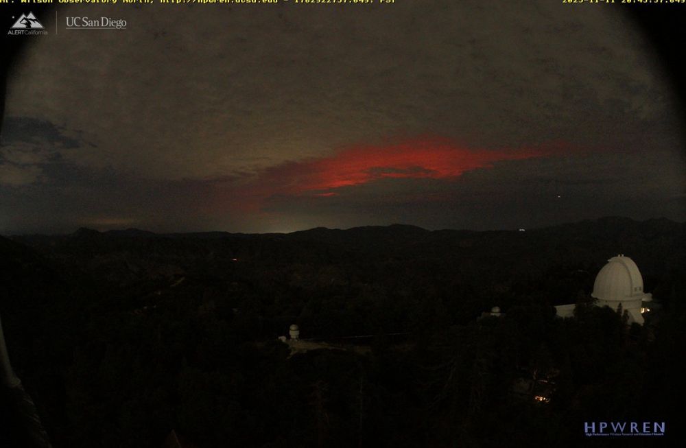 A view of the sky looking north from Mt. Wilson Observatory showing a deep red aurora visible in the break in the clouds.