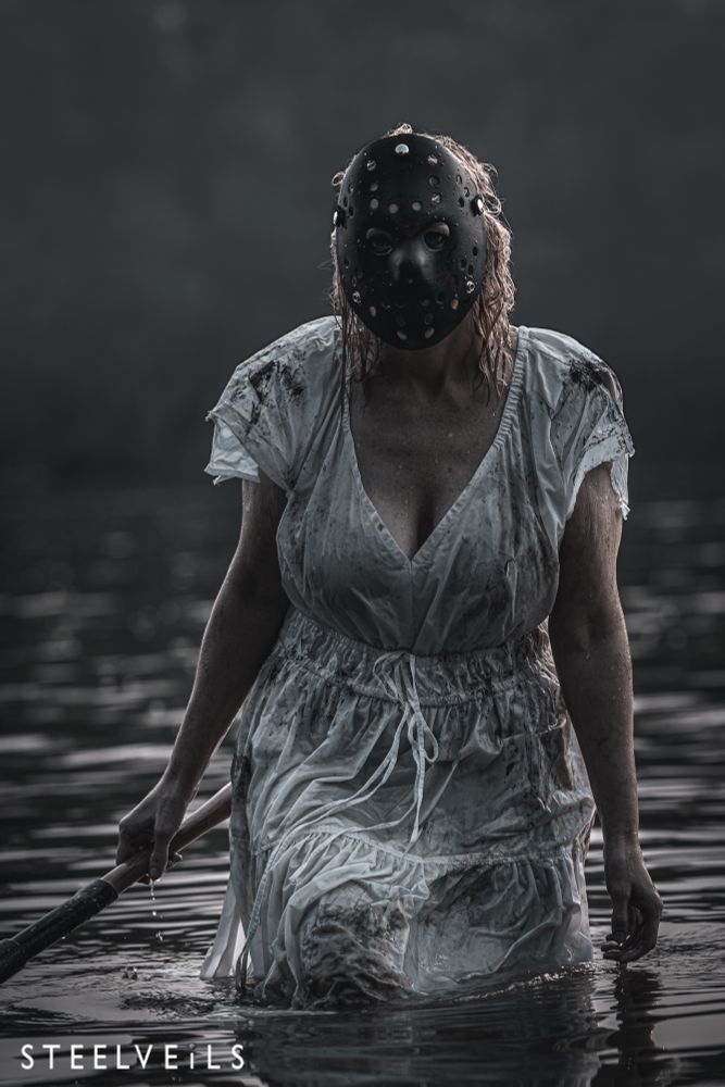 Blonde girl with white dress, dirty, wearing a hockey mask, walking out of a lake, carrying an axe. 