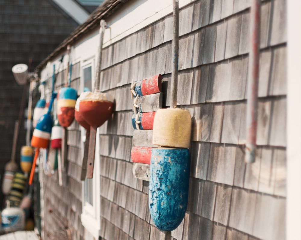 Old, colorful buoys hanging from a shingled wall. 