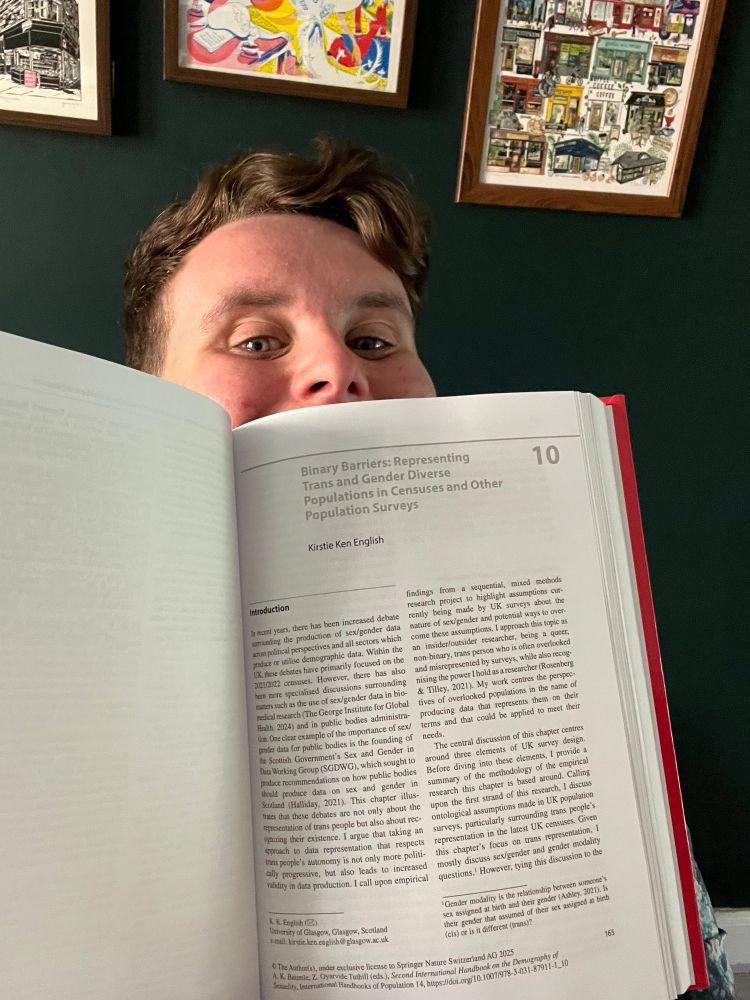 Kirstie Ken smiling behind an open copy of the book showing their chapter 
