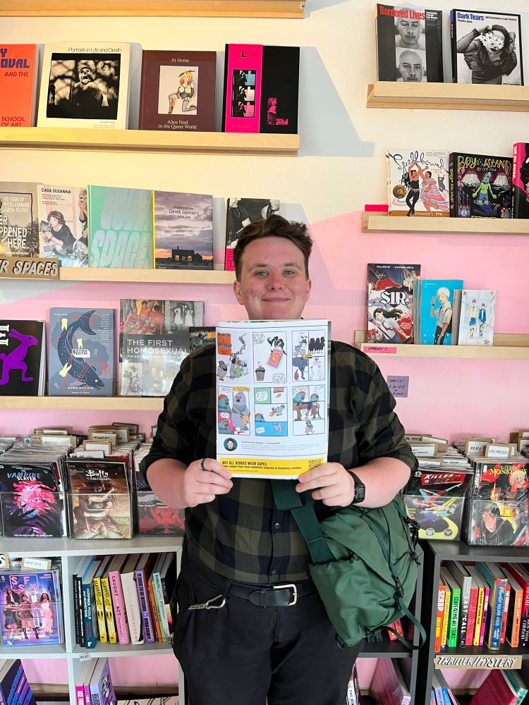 Kirstie Ken a white persona with short brown hair in a green checked shirt holding a magazine with a comic strip showing. 