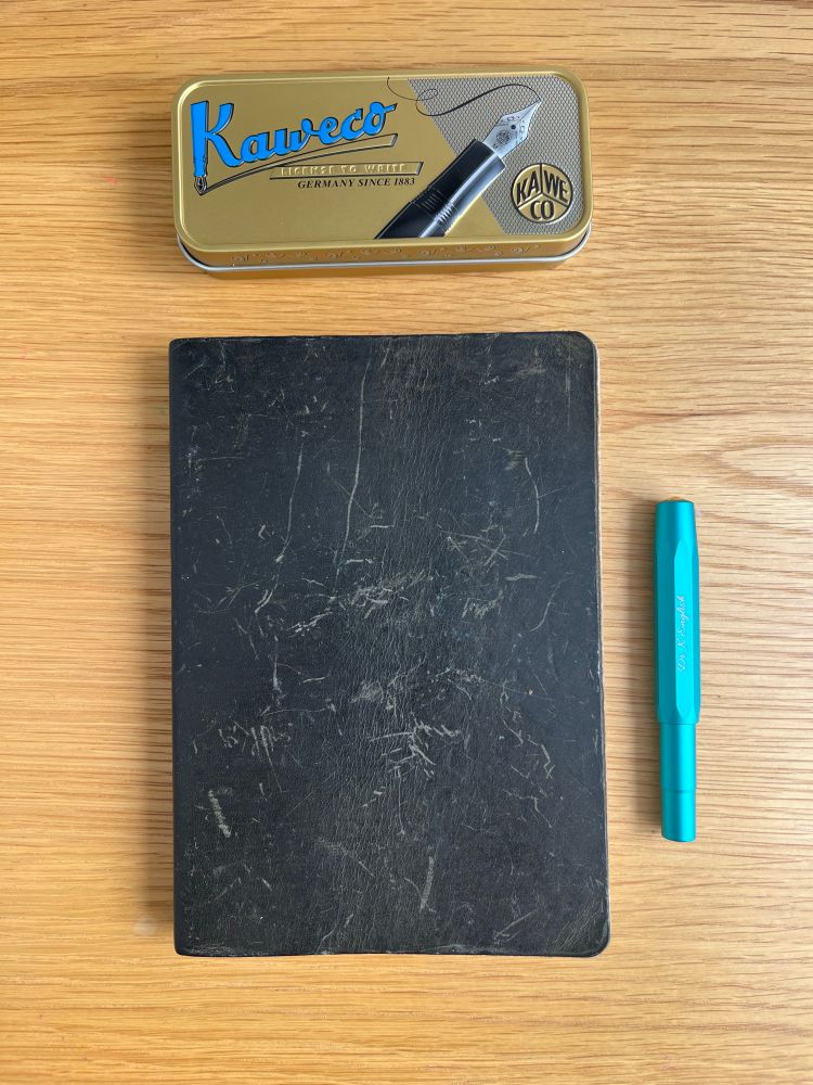 A dark green leather journal next to a metal fountain pen