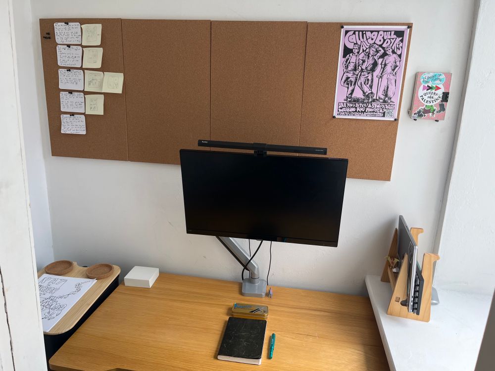 A very small box room office with a pin board behind a desk with a monitor 