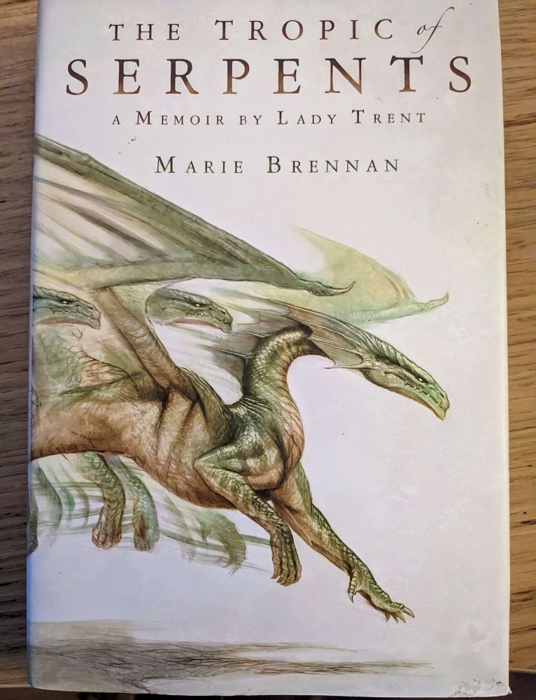 A cover of a book titled "The Tropic of Serpents: A Memoir by Lady Trent" written by Marie Brennan. The cover image shows a green dragon drawn in movement leaping and landing on the ground.