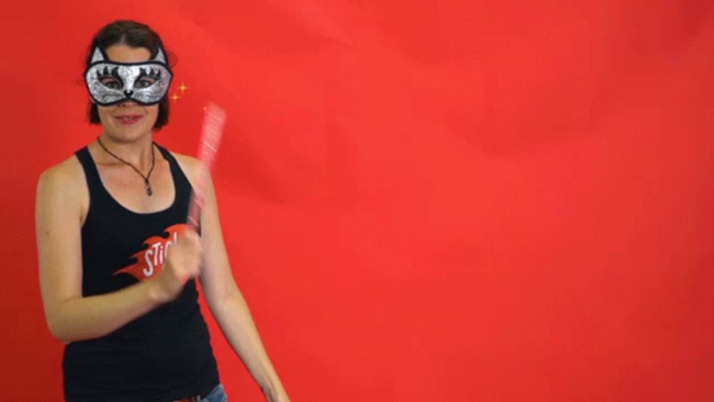 a woman wearing a mask holds a wand in front of a red background with five stars