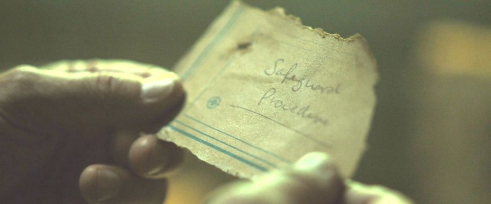Screen capture from the Silo TV show. A ripped piece of paper held with two hands that says Safeguard Procedure on it.