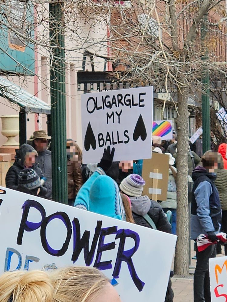 Crowd of protesters with signs in Colorado Springs, faces blurred for privacy.

A person in a teal hoodie holds up my favorite sign of the day, which says OLIGARGLE MY BALLS