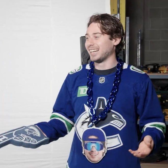 Quinn smiling with a chain around his neck and a foam finger. He is in the locker room. 