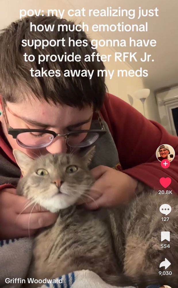 A person kissing their cat and the cat looks alarmed. The text above the cat reads “pov: my cat realizing just how much emotional support he’s gonna have to provide after RFK Jr takes away my meds.”