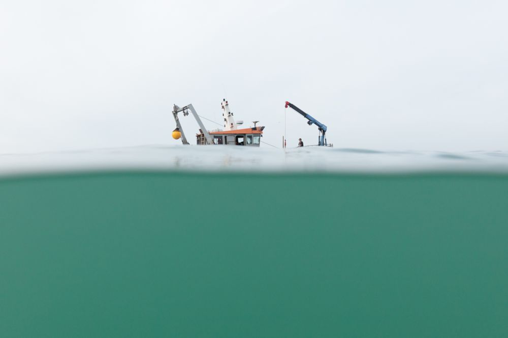A passing boat, as seen from a swimmers perspective and appearing partially submerged behind the swell. The boat is the 'Valkyrie' which scoots along the coast at the start and end of the swimming season in Brighton & Hove and deposits/scoops up the 'Swim Area' buoys. As far as I know, it's still very much afloat.