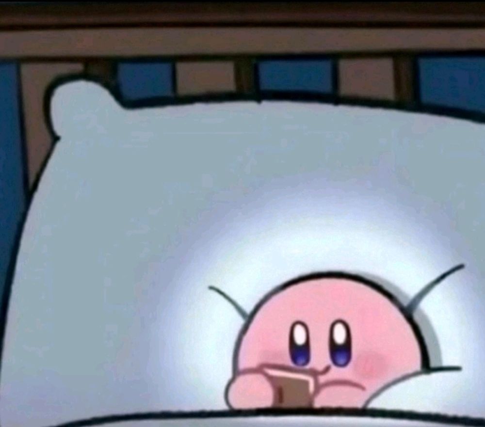 Image of Kirby laying on a big pillow as they scroll through some electronic device