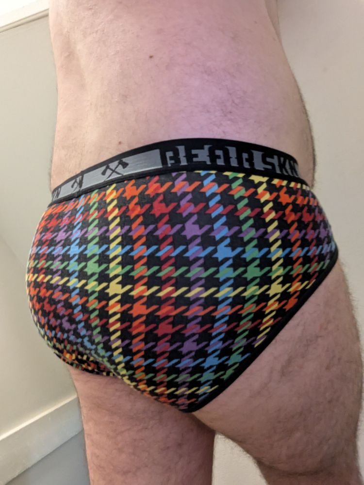 Photo of me wearing the black-rainbow-houndstoooth briefs and nothing else. I'm reaching behind myself to take the photo at an angle that shows off the curves of my butt.