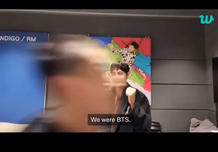 V stands in a "fighting" mode as Jung Kook speeds past the camera after getting his hair cut for military service.