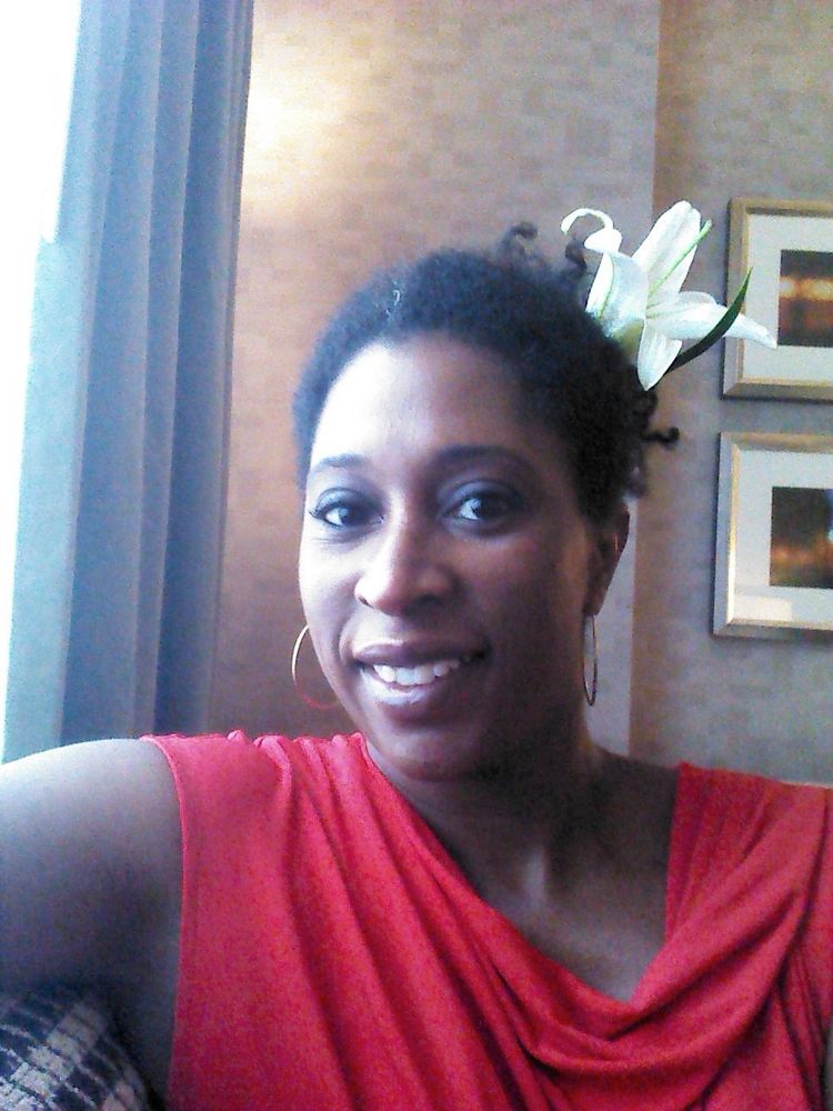 African American woman, sitting.  in a red dress. Gardenia in her hair. Soft smile