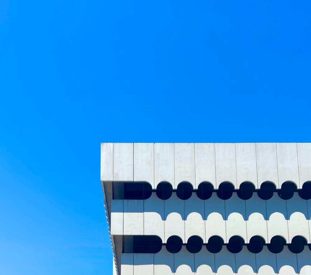 View of the top of a white, modern building against a blue sky.