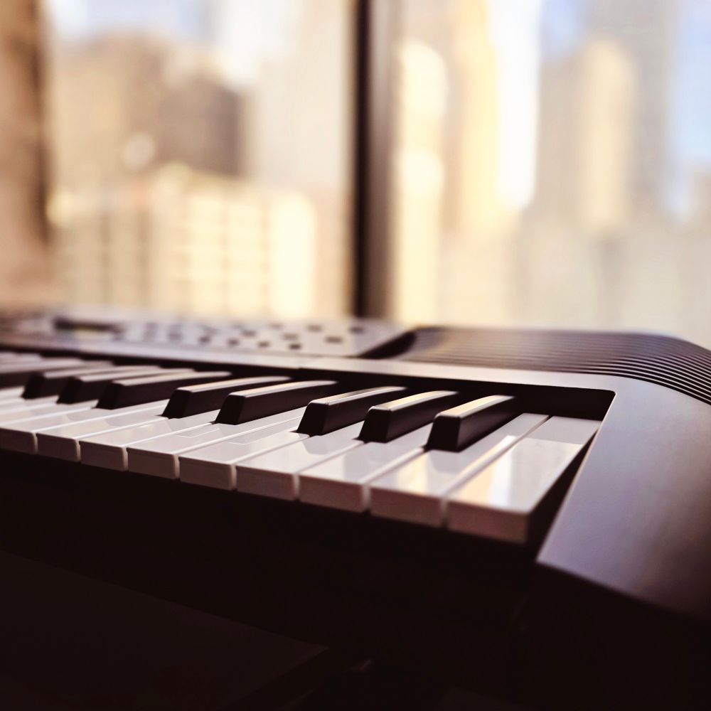 Close up photo of an electronic keyboard in front of a window overlooking skyscrapers.