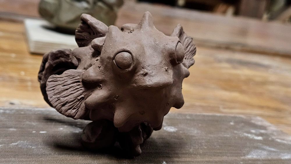 A small puffer fish with an overbite made out of black clay, propped up to dry.