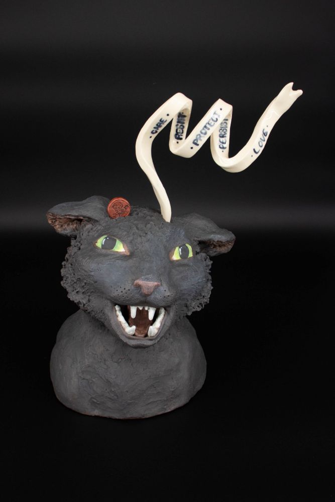 A hissing cat sculpture has a penny dropping into one side of their head and a ribbon of thoughts winding out of the other side, reading Care Resist Protect Persist Love.