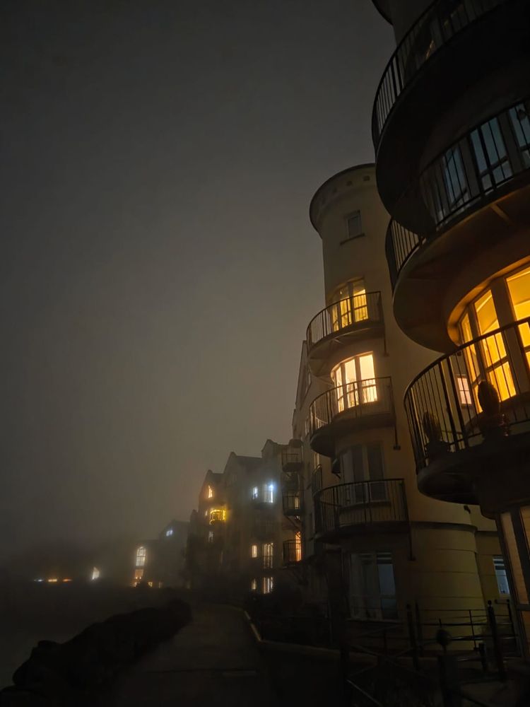 Glowing apartment windows in deep fog.