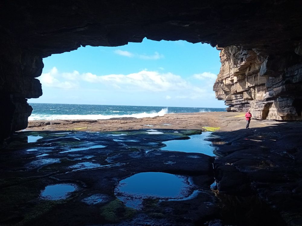 A view from inside a beautiful sea cave with sunshine outside and the sky reflected in pools inside 