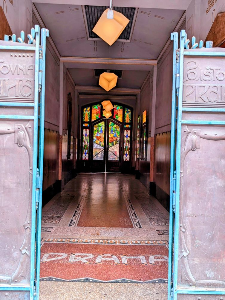 A corridor with stain glass in the back, Praha written as a floor mosaic in art nouveau style.
