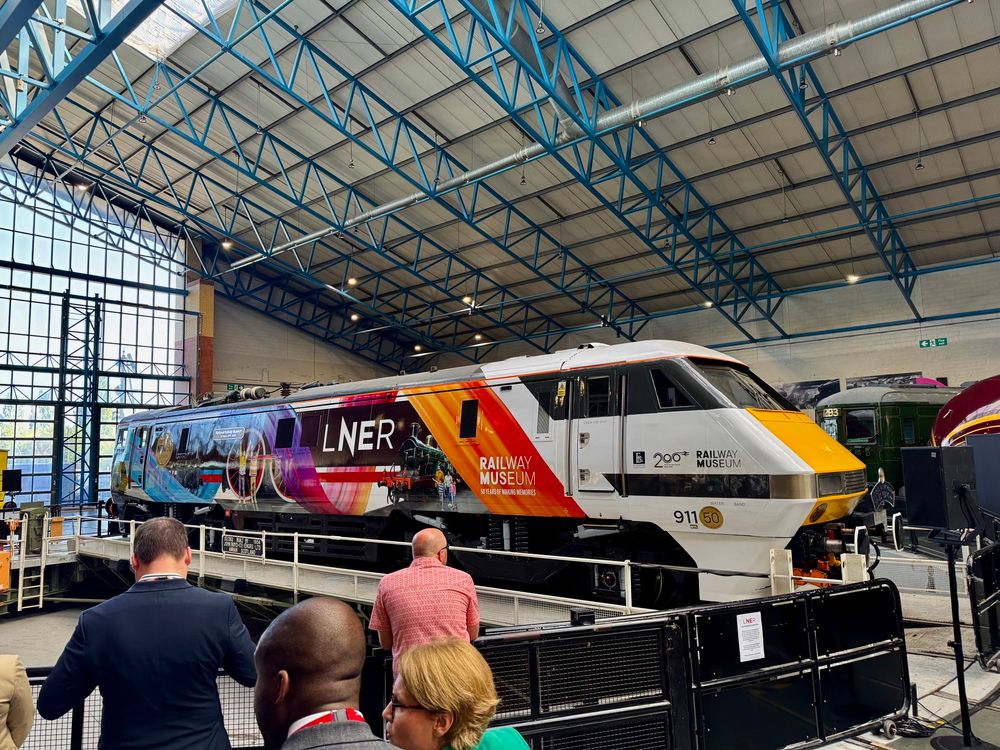 A Class 91 locomotive wearing a bright livery design of multicoloured ribbons and photographs of trains in the National Railway Museum collection, on a turntable in the main exhibition hall of the National Railway Museum in York. 