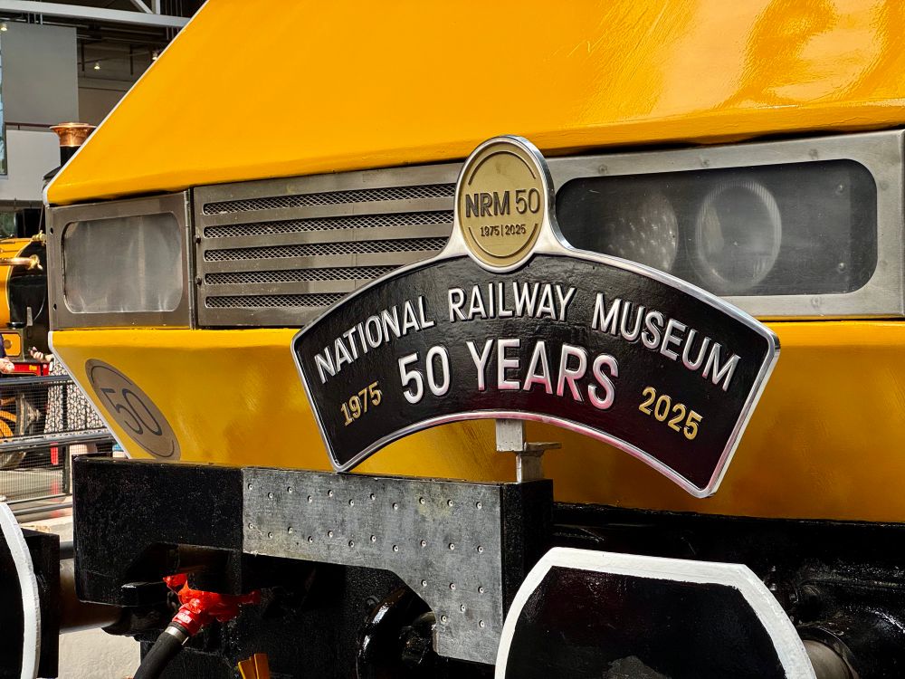 A close up view of the front of a Class 91 locomotive carrying a cast steel headboard reading "National Railway Museum 50 Years 1975-2025".