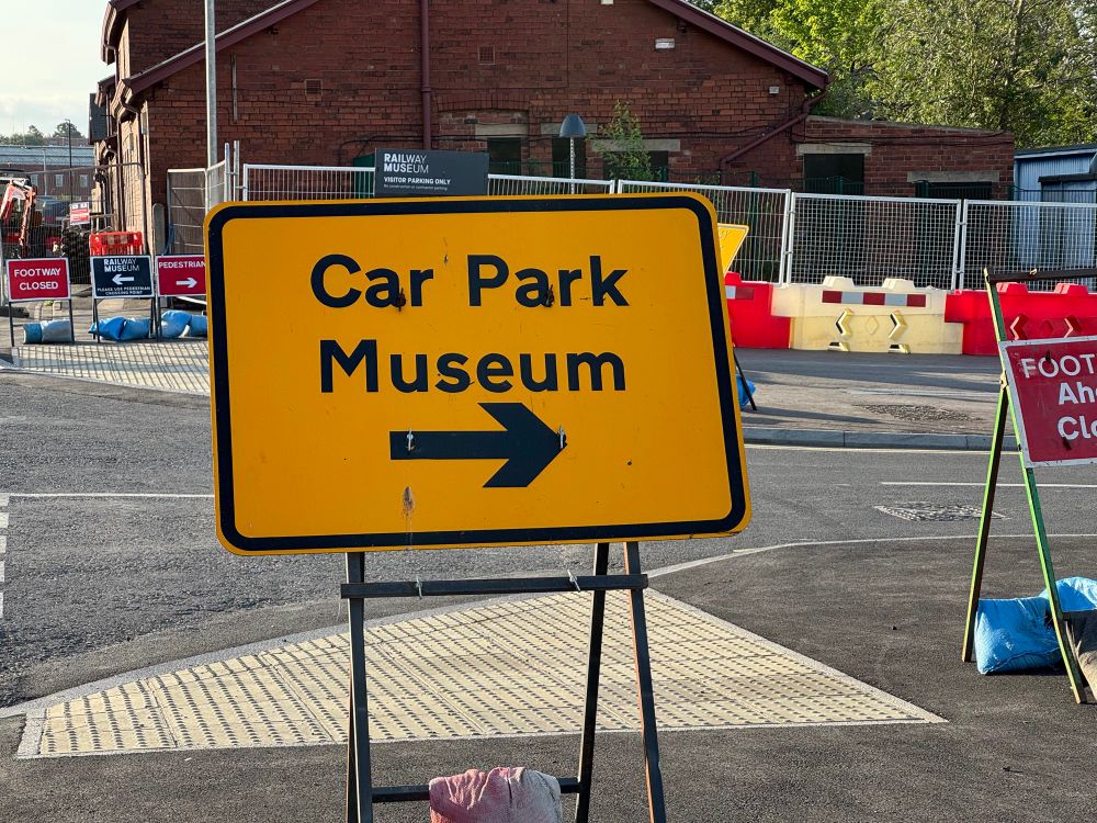 A yellow temporary street sign with black text "Car Park Museum" and a black arrow pointing to the right. 