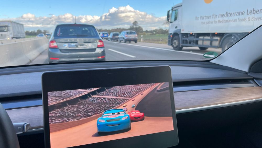 Blick aus unserem Tesla Model 3 auf den Stau, auf dem großen Display läuft gerade der Trickfilm Cars 3