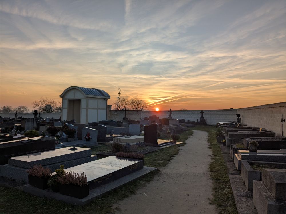 Cimetière d'Auvers sur Oise au coucher du soleil juste au-dessus du mur d'enceinte. À droite, le long du mur, les deux tombes des frères Van Gogh recouvertes de lierre. Une allée, d'autres tombes... 