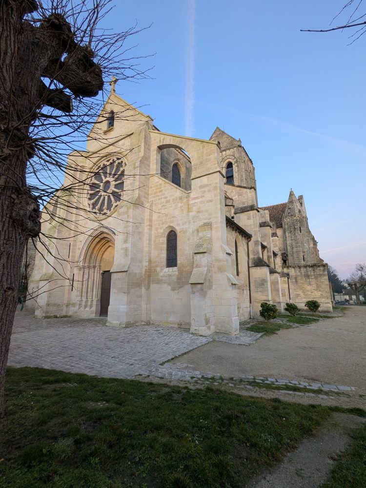Eglise d'Auvers sur Oise, la rosace au dessus du porche fin de journée , ciel bleu. Premier plan à gauche un bout d'arbre trogne. 
