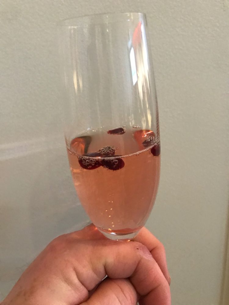 A glass of AEI sparkling rosé with pomegranate seeds in it.