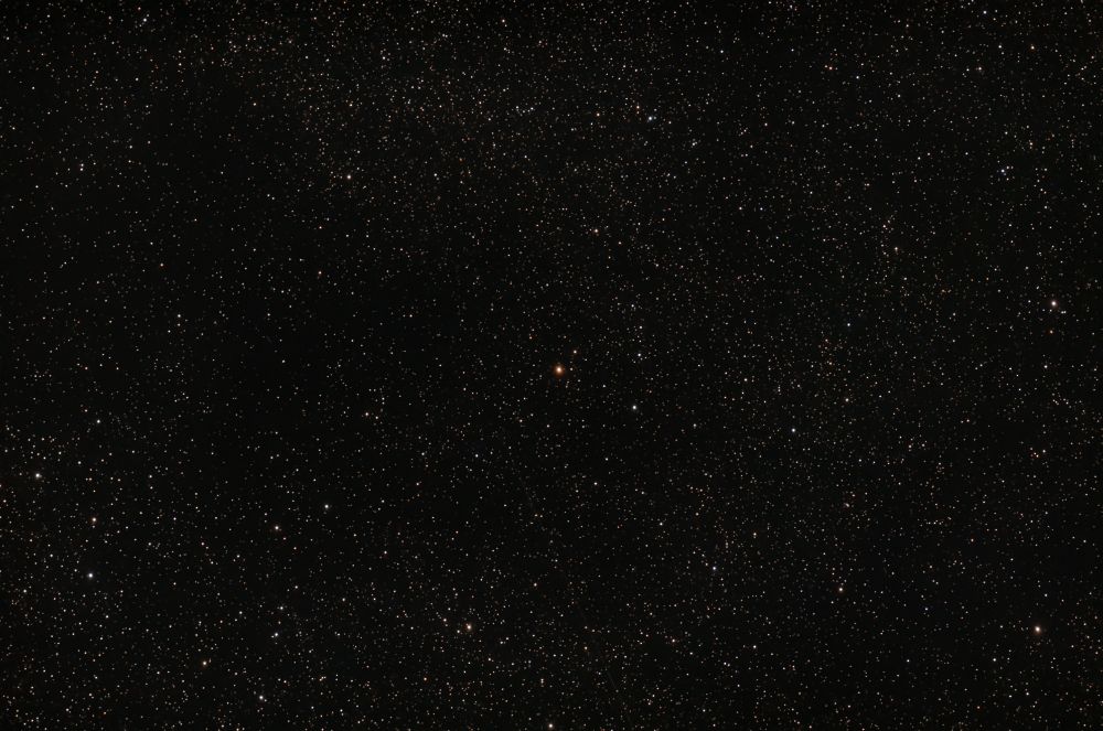 A telescopic image of a field of stars with a red star at center.