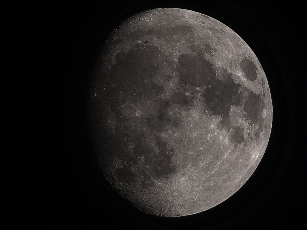 A telescopic image of the Moon in the waxing gibbous phase. Many bright impact craters, some with rays extending outward from them are visible along with large, dark round plains.