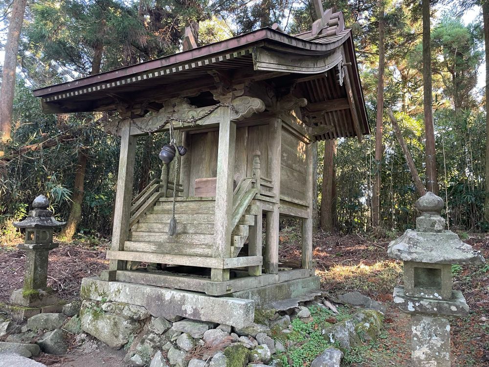 Small wooden shrine with bell at the top of Mt Ujidake: a foundation of stones and concrete, wooden steps, a rope attached to a bell, and a donation box.
