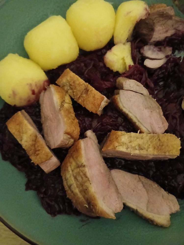Klöße mit Rotkohl Preiselbeere in Rotwein mit Entenbrust auf tiefen  Blauen/Grüne  Teller.