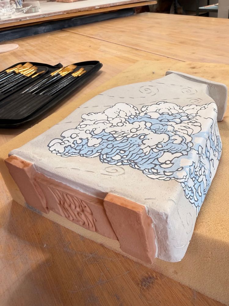 A bone dry clay vase lays on a table. It has stylized clouds painted on it. Wind trails are etched into the unpainted areas of the clay. On the underside of the vase is a stamp of the artist “Justin Groom”

#Ceramics #ClayArt #Pottery #Clay #ArtTherapy #AutisticArtist #ADHD #Sculpture #Art #Artist #Vase #Clouds