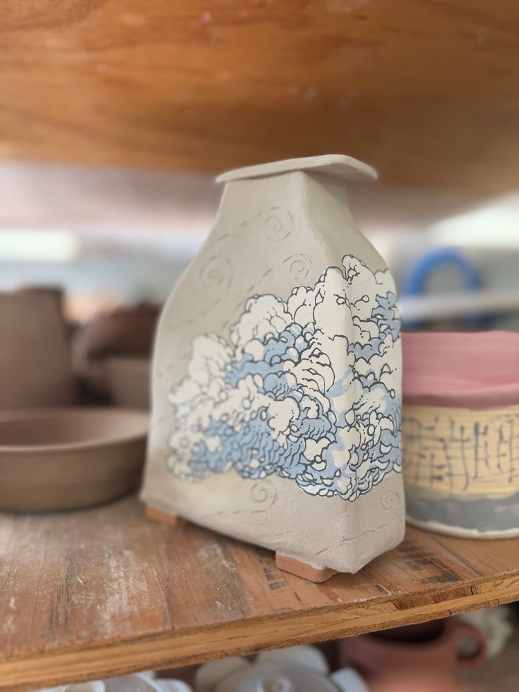 A bone dry clay vase sits on a shelf. It has stylized clouds painted on it. Wind trails are etched into the unpainted areas of the clay.

#Ceramics #ClayArt #Pottery #Clay #ArtTherapy #AutisticArtist #ADHD #Sculpture #Art #Artist #Vase #Clouds