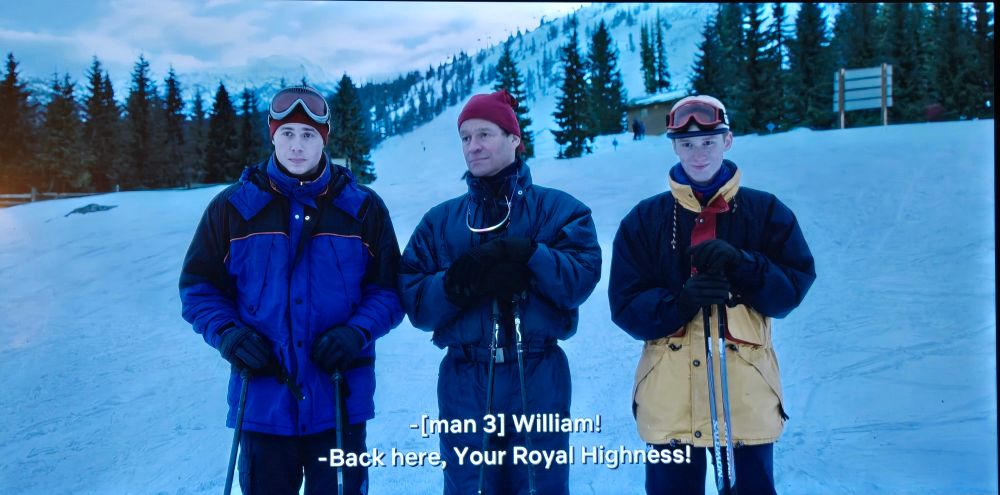Actors playing Prince William, Prince Charles, and Prince Harry in ski outfits at what appears to be a ski hill at Whistler, British Columbia, Canada.