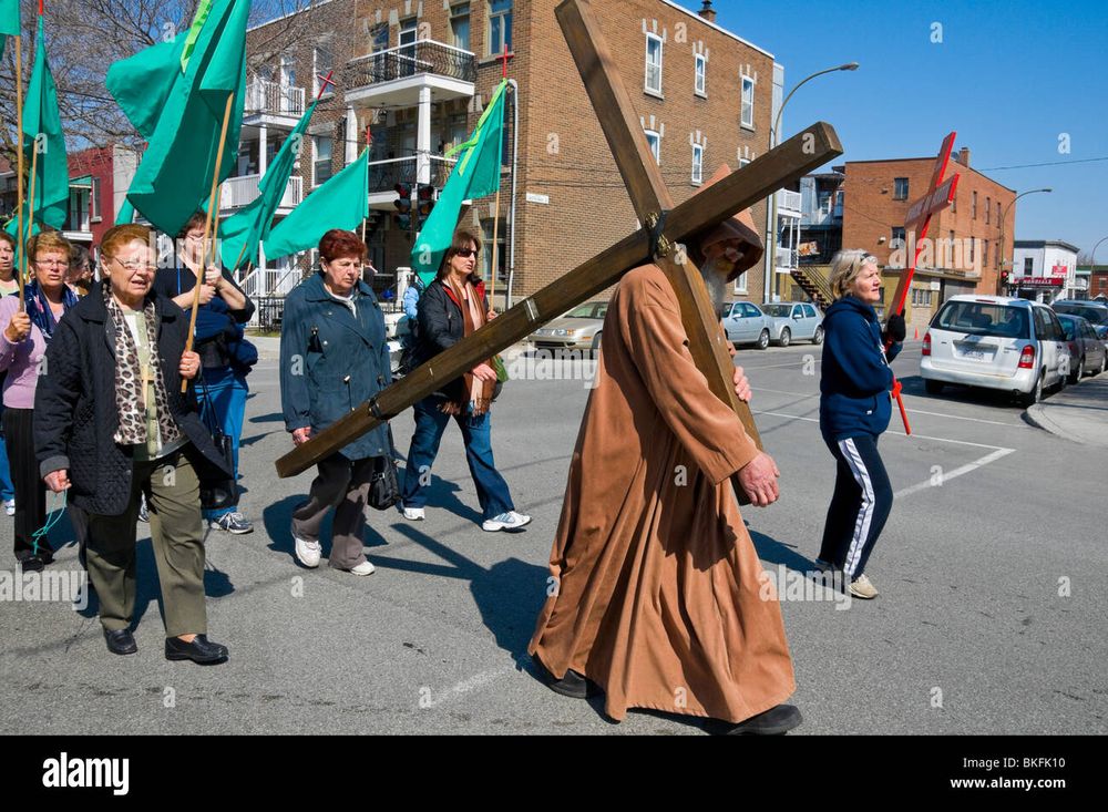 Good Friday parade in Montreal. A man is carrying a large cross. People behind are holding green flags. A woman to the side is holding a smaller cross.