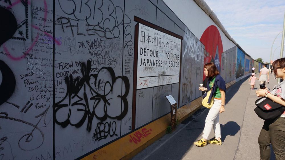 East Side Gallery in Berlin. It consists of the wall still erect to show its history. A tourist looks at a painting that states, "Detour to the Japanese Sector." 2013