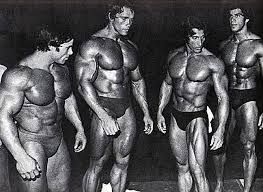 Arnold Schwarzenegger as a bodybuilder stands with three other bodybuilders. Note: Arnold Schwarzenegger is not gay.
