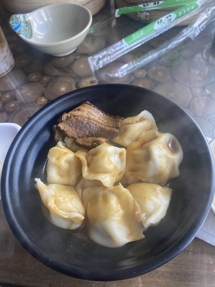 a bowl with dumplings in soy chili oil and a piece of roasted pork