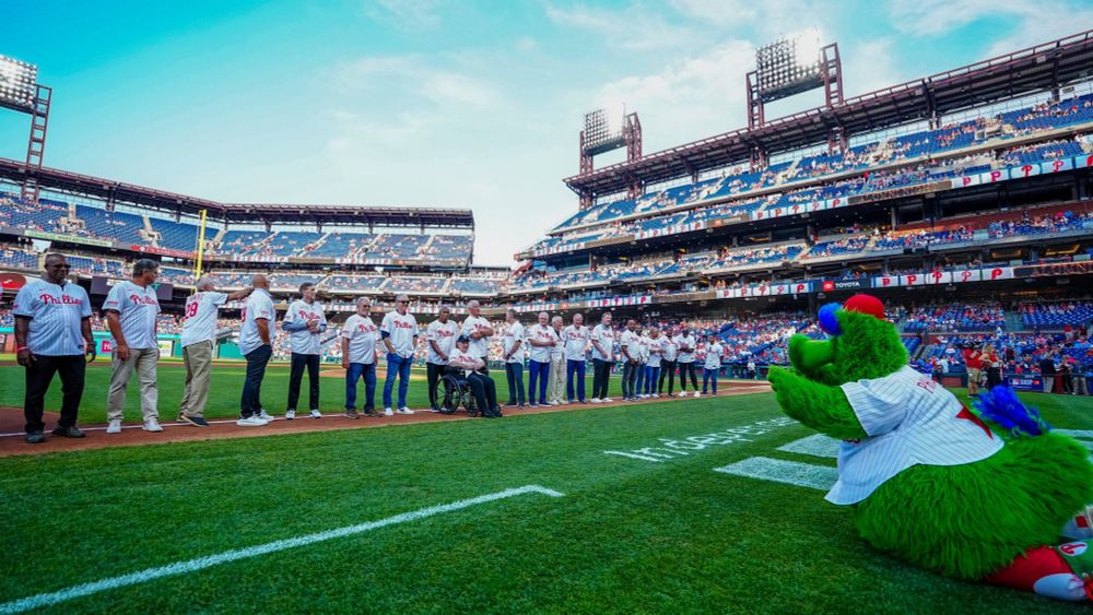 The Phillies Phanatic bows as the group of Phillies alumni stands on the third base line during tonight's pregame ceremony.