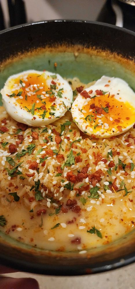 picture of chicken ramen with sesame seeds, a soft boiled egg, parsley, tajin, and bacon bits.