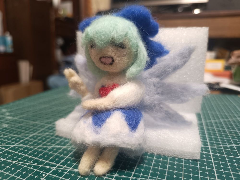 Doll made out of wool of blue haired fairy girl with ice wings. She shows peace sign with right hand